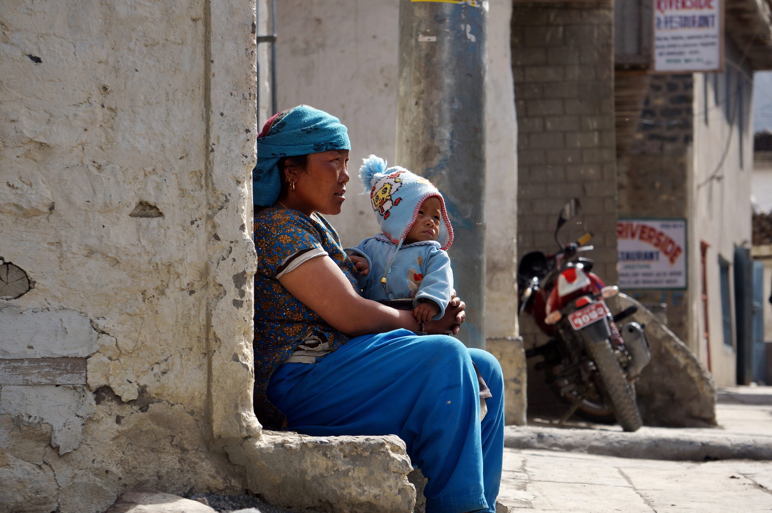 An unidentified Nepalese woman with a small child on her knees sits against the wall of a house on Jomsom Street. Nepal.